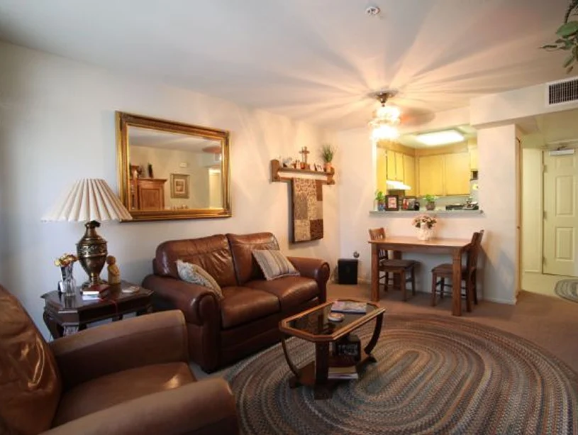 Warm senior apartment with leather seating, dining table, and open kitchen, decorated with cozy lighting, mirror, and wall art.
